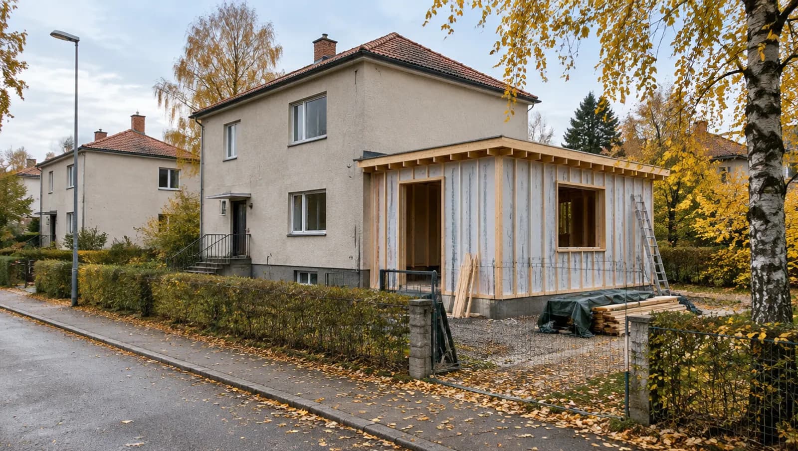 Funkisvilla på en förortsgata på hösten med en ny tillbyggnad i trä under uppförande